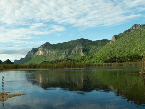 Rock cliff and green forest in lake with blue sky and white could in background, Reflection of Limestone mountain on water of the vast wetland at Khao Sam Roi Yot National Park , Thailand