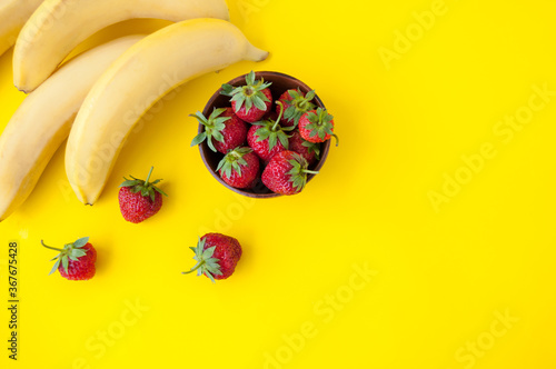 Strawberries in a clay Cup bananas on a yellow background, place for text, top view