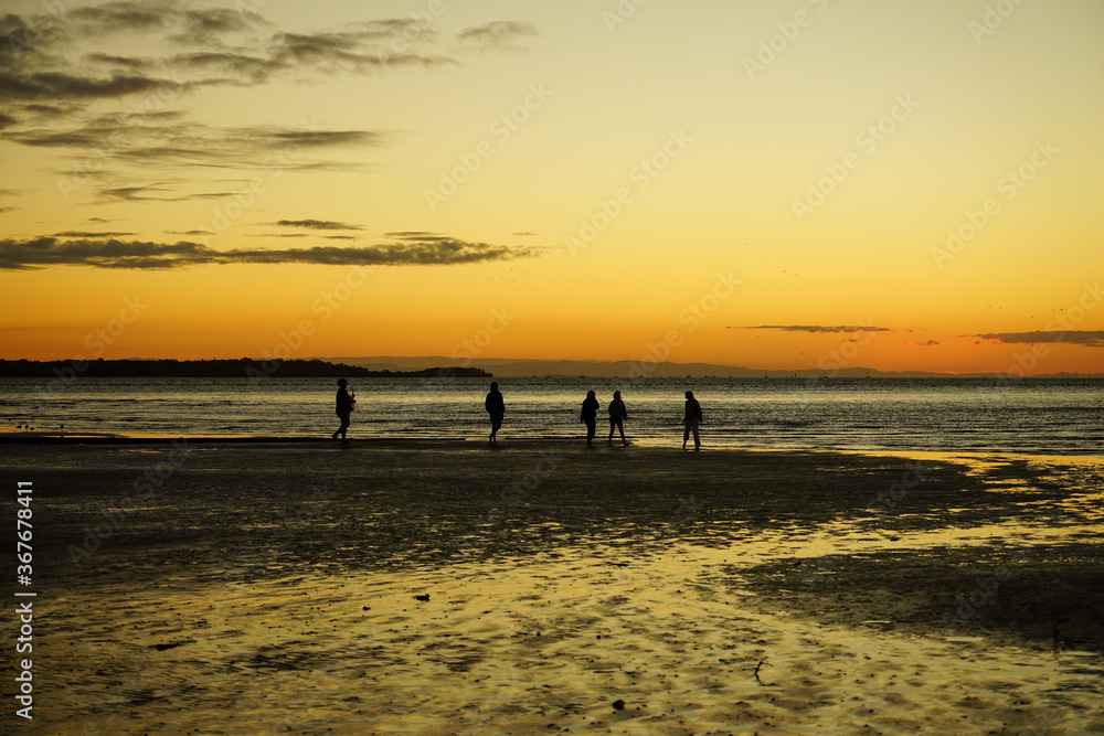 Golden glow of sunset on the beach at low tide, with silhouette of five people in the distance. Dunwich, North Stradbroke Island, Queensland, Australia.	