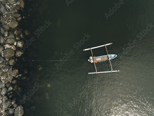 Top view of small wooden boat anchored with rope on transparent water with stones