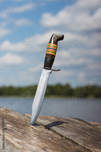 Hunting knife stuck in the boards on the background of the lake