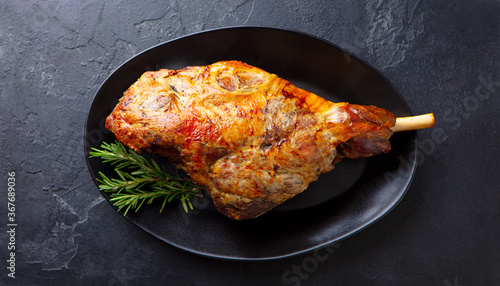 Fototapeta Naklejka Na Ścianę i Meble -  Roasted lamb leg on a plate. Black background. Close up. Top view.