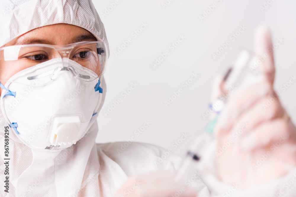 Asian female woman doctor or nurse in PPE uniform and gloves wearing face mask protective in the laboratory holding needle syringe drug and medicine vial vaccine bottle, Health medical concept Asian female woman doctor or nurse in PPE uniform and gloves wearing face mask protective in the laboratory holding needle syringe drug and medicine vial vaccine bottle, Health medical concept