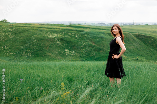 Young beautiful girl with dark hair in a dress outdoors. Everything is green around. Happy girl. Environment concept, nature