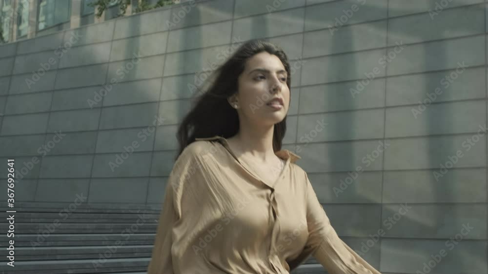 Beautiful Hispanic Young adult business woman walking to office in city with wind blowing in long hair Beautiful Hispanic Young adult business woman walking to office in city with wind blowing in long hair