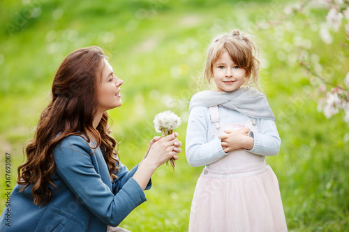 Mother with small daughter blowing to dandelion - lifestyle outdoors scene in park. Happy family concept © fadzeyeva