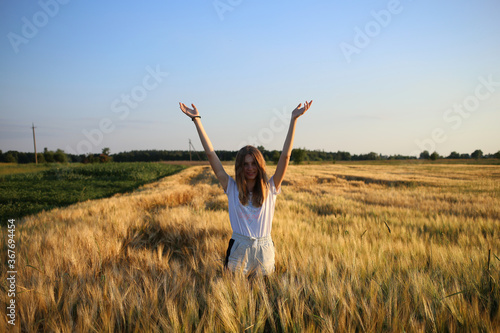 Happy girl with raised hands posing in a barley field, on a summer evening.
