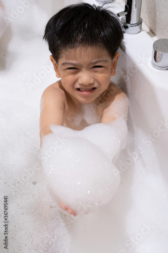 Happy asian boy taking a bath playing with foam bubbles in bathtub.