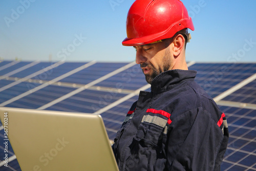 Electrician in a red helmet and laptop in the solar power plant, green energy