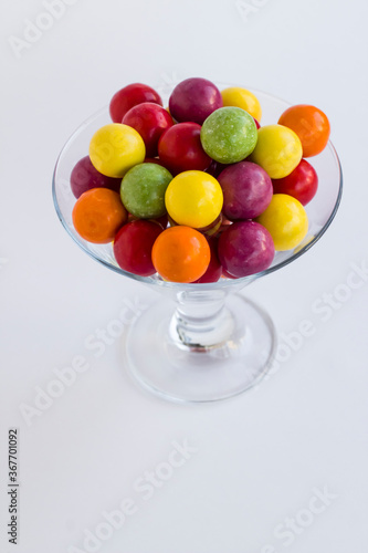 Colorful candies in transparent glass bowl on grey background.