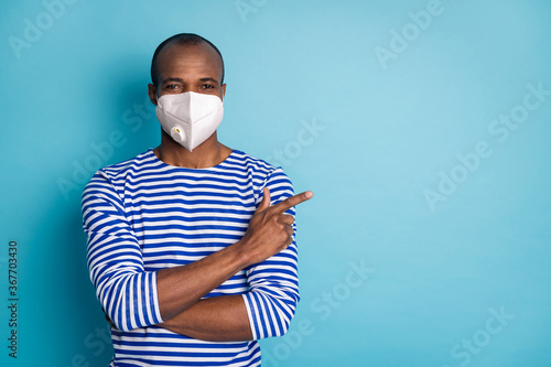 Portrait of his he content healthy guy wearing safety trendy n95 respirator mask demonstrating copy empty space stop mers cov influenza flu grippe isolated over blue color background photo