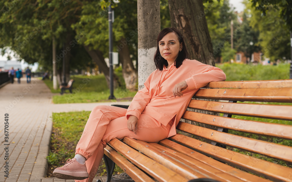 Young woman sits on bench in park. Adult female enjoys her rest on fresh air. Young woman sits on bench in park. Adult female enjoys her rest on fresh air.