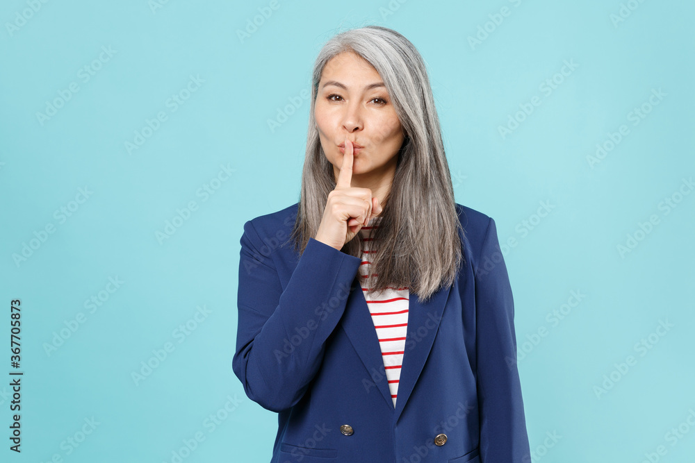 Secret gray-haired business woman in blue suit isolated on blue background studio. Achievement career wealth business concept. Mock up copy space. Say hush be quiet with finger on lips shhh gesture. Secret gray-haired business woman in blue suit isolated on blue background studio. Achievement career wealth business concept. Mock up copy space. Say hush be quiet with finger on lips shhh gesture.