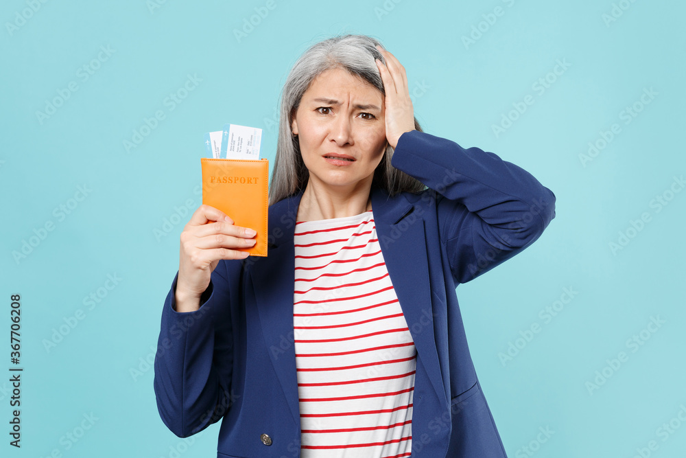 Preoccupied worried gray-haired business woman in blue suit posing isolated on blue background. Achievement career wealth business concept. Mock up copy space. Hold passport tickets put hand on head. Preoccupied worried gray-haired business woman in blue suit posing isolated on blue background. Achievement career wealth business concept. Mock up copy space. Hold passport tickets put hand on head.