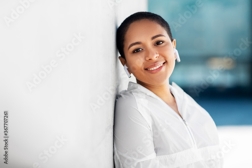 fitness, sport and technology concept - happy smiling young african american woman with wireless earphones listening to music outdoors