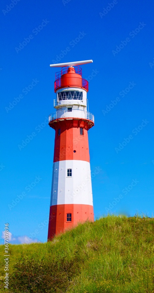 Wunderschöner rot weiß gestreifter Leuchtturm auf der Insel Borkum  vor strahlend blauem Himmel in den Dünen.