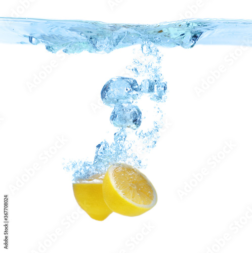 Cut lemon falling down into clear water against white background