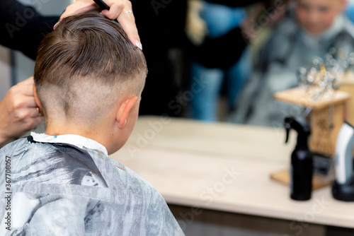 Back view Close up caucasian pretty school boy trendy haircut at bright modern barbershop.