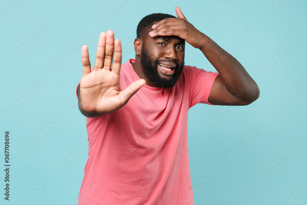 Worried young african american man guy in casual pink t-shirt posing isolated on pastel blue background. People lifestyle concept. Mock up copy space. Showing stop gesture with palm, put hand on head. Worried young african american man guy in casual pink t-shirt posing isolated on pastel blue background. People lifestyle concept. Mock up copy space. Showing stop gesture with palm, put hand on head.