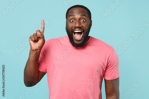 Excited young african american man guy in casual pink t-shirt isolated on blue background studio portrait. People lifestyle concept. Mock up copy space. Holding index finger up with great new idea.