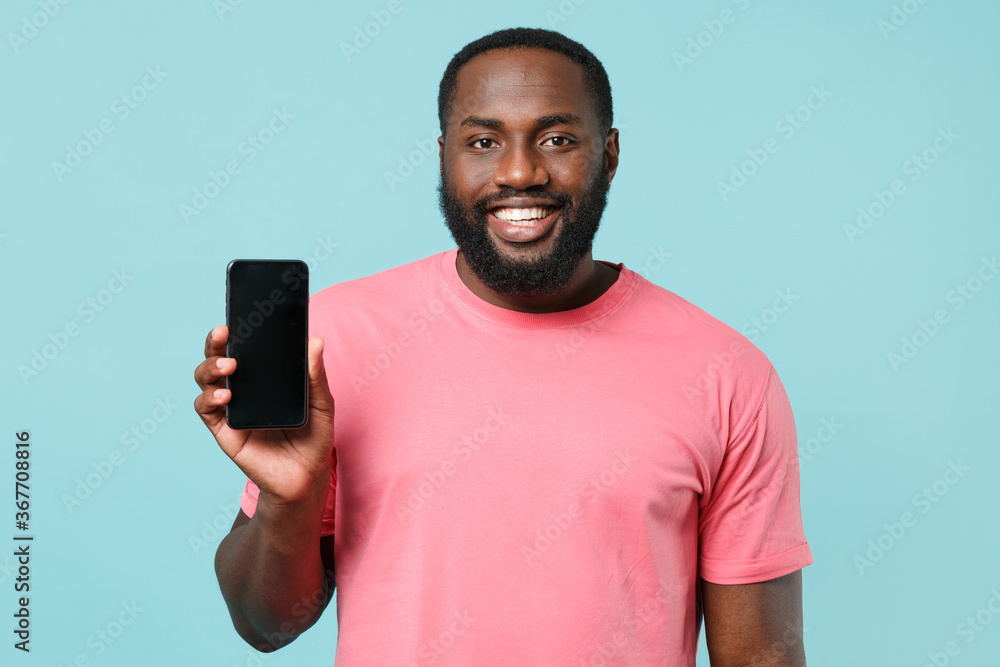 Smiling young african american man guy in casual pink t-shirt isolated on blue wall background studio portrait. People lifestyle concept. Mock up copy space. Hold mobile phone with blank empty screen. Smiling young african american man guy in casual pink t-shirt isolated on blue wall background studio portrait. People lifestyle concept. Mock up copy space. Hold mobile phone with blank empty screen.