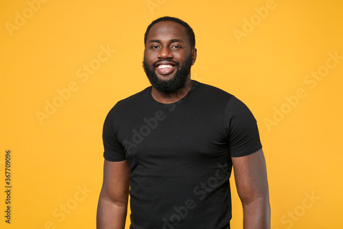 Smiling african american man guy football fan in casual black t-shirt isolated on yellow wall background studio portrait. People sincere emotions lifestyle concept. Mock up copy space. Looking camera.