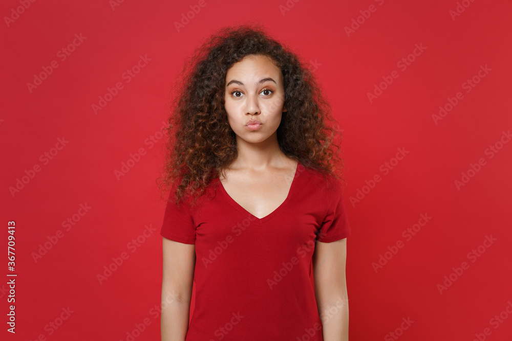 Pretty young african american woman girl in casual t-shirt posing isolated on red background studio portrait. People emotions lifestyle concept. Mock up copy space. Blowing lips, making duck face. Pretty young african american woman girl in casual t-shirt posing isolated on red background studio portrait. People emotions lifestyle concept. Mock up copy space. Blowing lips, making duck face.