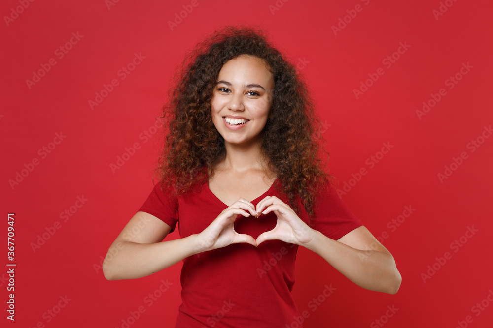 Smiling young african american woman girl in casual t-shirt posing isolated on red background studio. People lifestyle concept. Mock up copy space. Showing shape heart with hands, heart-shape sign. Smiling young african american woman girl in casual t-shirt posing isolated on red background studio. People lifestyle concept. Mock up copy space. Showing shape heart with hands, heart-shape sign.