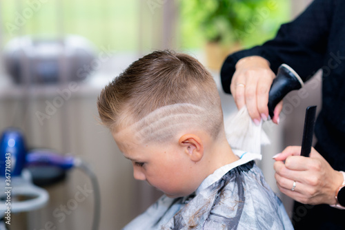 Side view caucasian american pretty school boy after haircut done stylish hairstyle wipes the hair at bright barbershop.