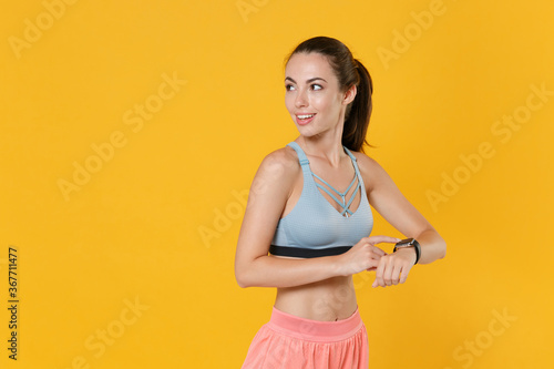 Smiling young fitness sporty woman in sportswear working out isolated on yellow background. Workout sport motivation lifestyle concept. Mock up copy space. Wearing smart watch on hand, looking aside. © ViDi Studio