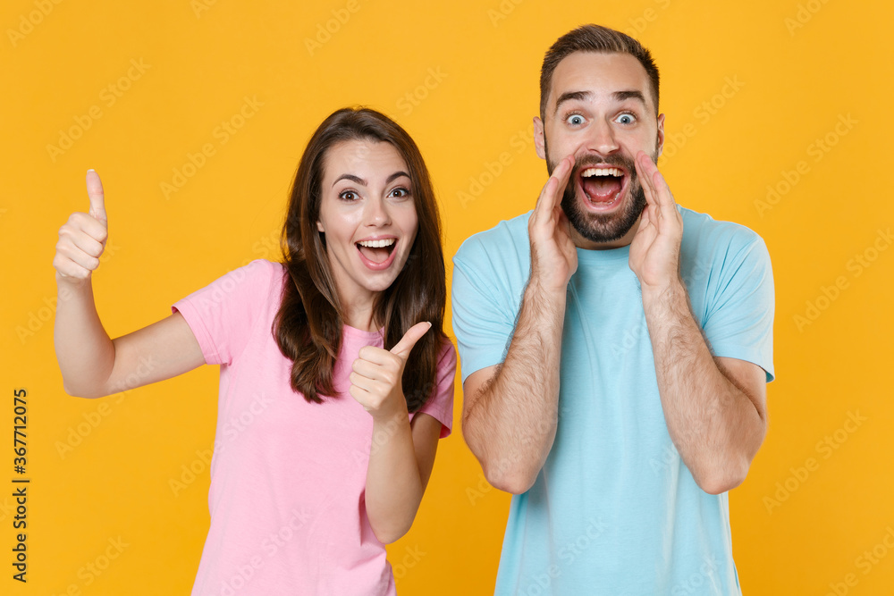 Excited young couple two friends guy girl in blue pink t-shirts isolated on yellow background. People lifestyle concept. Mock up copy space. Screaming with hands gesture near mouth, showing thumbs up. Excited young couple two friends guy girl in blue pink t-shirts isolated on yellow background. People lifestyle concept. Mock up copy space. Screaming with hands gesture near mouth, showing thumbs up.