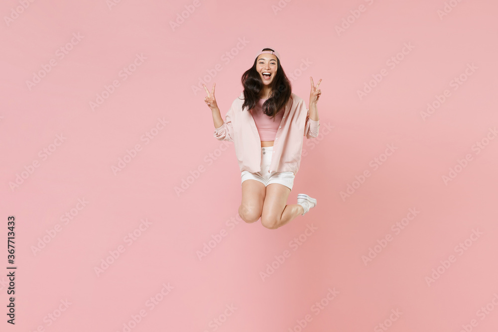 Full length portrait of cheerful young asian girl in casual clothes, cap isolated on pastel pink background studio portrait. People lifestyle concept. Mock up copy space. Jumping showing victory sign. Full length portrait of cheerful young asian girl in casual clothes, cap isolated on pastel pink background studio portrait. People lifestyle concept. Mock up copy space. Jumping showing victory sign.