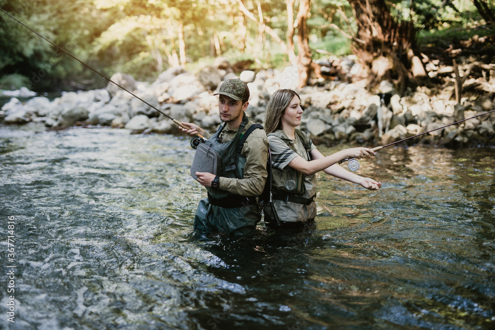 Young adult couple is fishing together on fast mountain river. Active people and sport fly fishing concept. Young adult couple is fishing together on fast mountain river. Active people and sport fly fishing concept.