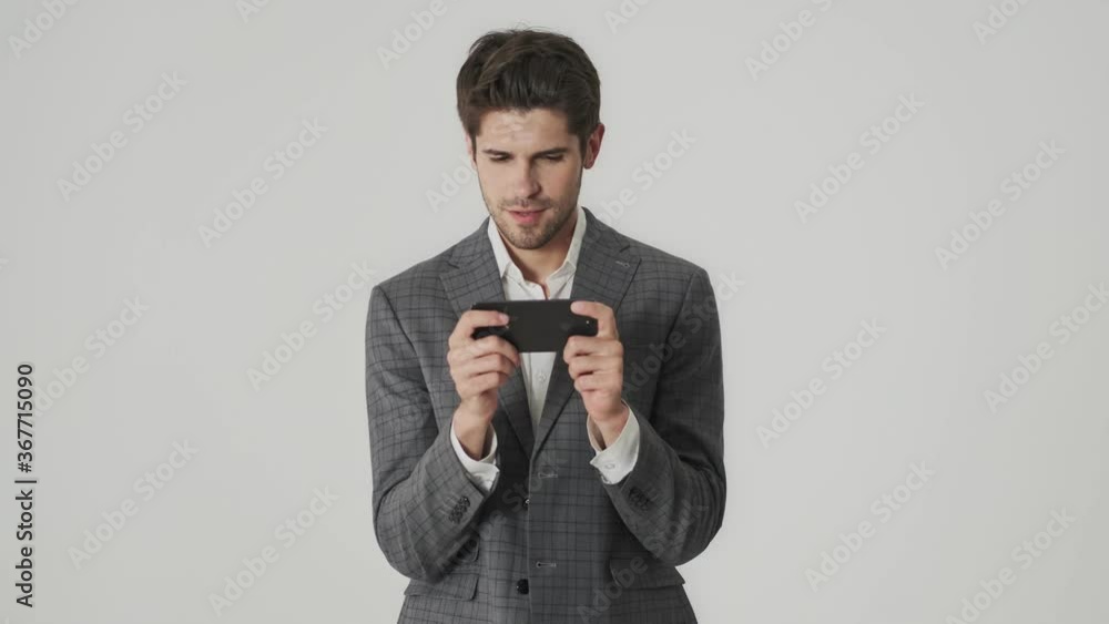 Concentrated business man isolated over white wall background while playing games by mobile phone Concentrated business man isolated over white wall background while playing games by mobile phone