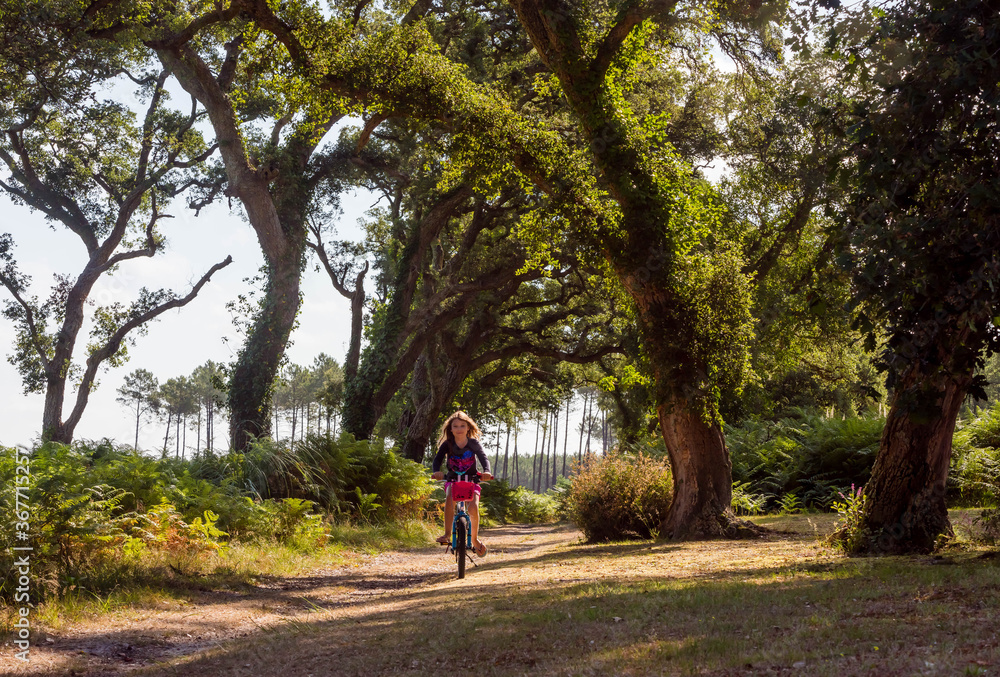 cute little girl riding a bicycle in a cork oak forest