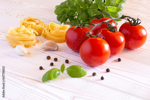 Raw tagliatelle pasta with fresh basil, garlic and tomatoes on a rustic white table, Copy space