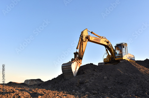 Excavator working on earthmoving at open pit mining. Yellow Backhoe digs sand and gravel in quarry. Heavy Construction Equipment Machines in Action. Digger during excavation at construction site.