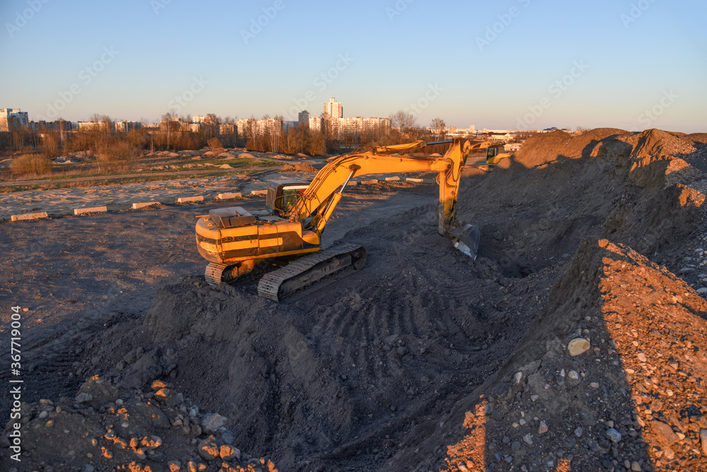 Excavator work at constrruction site on sunset background. Backhoe digs gravel and old concrete. Recycling old asphalt at a landfill for the disposal of construction waste. Construction machinery Excavator work at constrruction site on sunset background. Backhoe digs gravel and old concrete. Recycling old asphalt at a landfill for the disposal of construction waste. Construction machinery