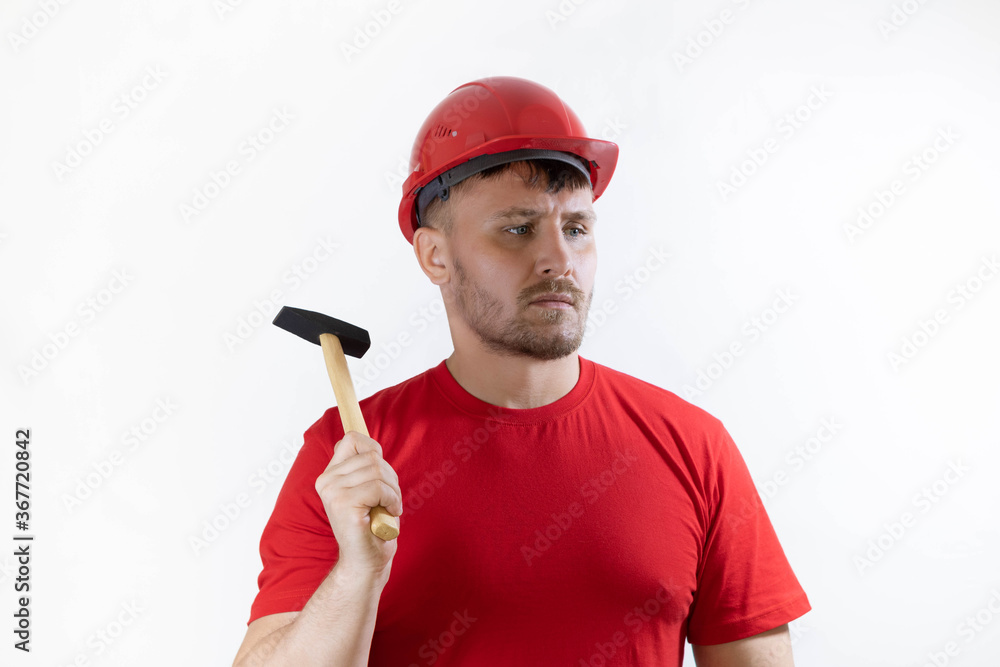 A man in a helmet and a red T-shirt holds a hammer in his hands.