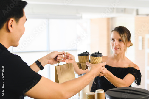 Barista giving bag and paper cups with hot drinks to customer at coffee shop