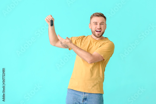 Happy young man with car key on color background photo