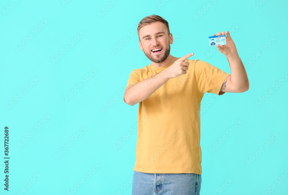 Happy young man with driving license on color background