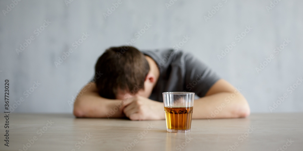 alcoholism concept - drunk man lying on the table and glass of whiskey over gray wall alcoholism concept - drunk man lying on the table and glass of whiskey over gray wall