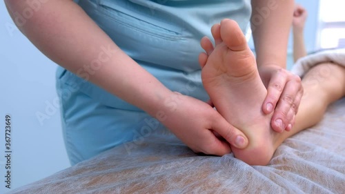 Doctor massagist making therapy massage to child boy on foot in clinic, closeup view. Dystrophy, muscle weakness, Morphan syndrome. Rehabilitation medicine, hypertonicity treatment for children. photo