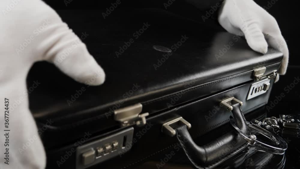 Mai in white gloves opens a briefcase full of gold bars. Handcuffed