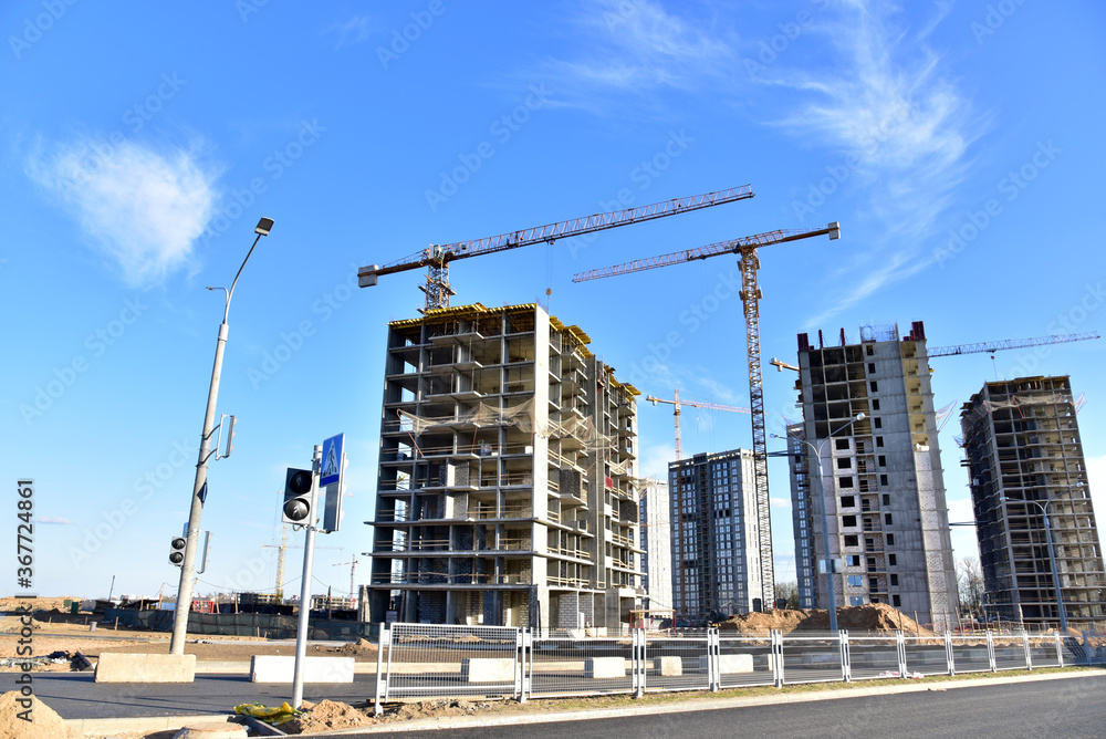 Tower cranes working at construction site on blue sky background. Construction process of the new modern residential buildings. Tall house renovation project, government programs.