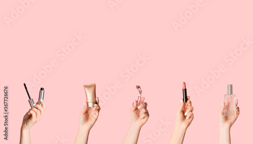 Women hands holding various cosmetic products on pink background, empty space. Creative collage