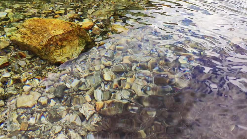 Water surface and colourful stones. Pure clean river water is running. Сlouds are reflected in the water. Water surface and colourful stones. Pure clean river water is running. Сlouds are reflected in the water.
