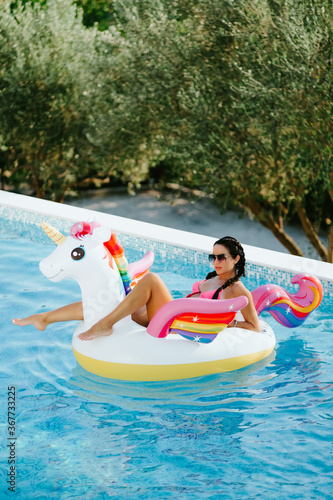 woman relax on inflatable pool toy unicorn in swimming pool. Sexy female in swimsuit on vacations relax on inflatable mattress in swimming pool outdoors with pool toys. Summer vacation time