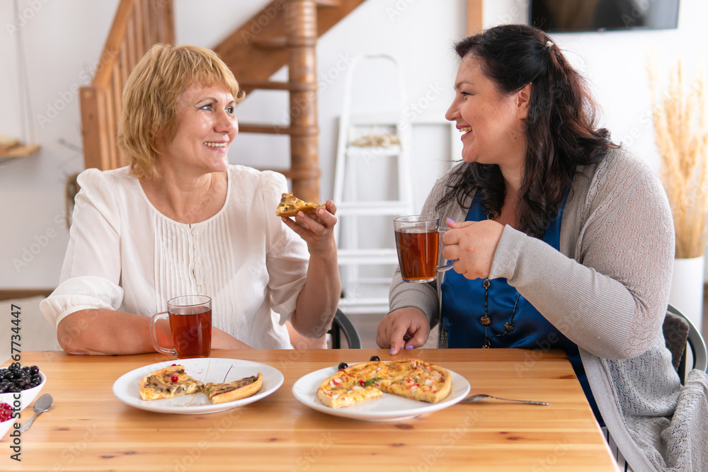 Women talk and eat pizza in the apartment. They're having a business lunch.